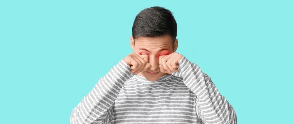 Young man rubbing eyes on light blue background